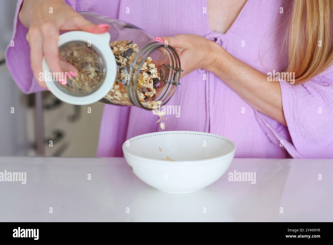 la colazione sana le mani femminili mettono la muesola fatta in casa in un piatto Foto Stock