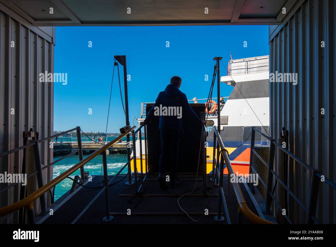 Una sagoma di un uomo in attesa di abbassare un passaggio pedonale per permettere ai passeggeri di salire e scendere dal traghetto presso il terminal dei traghetti di Devonport vicino Auckland, nuova Zelanda Foto Stock