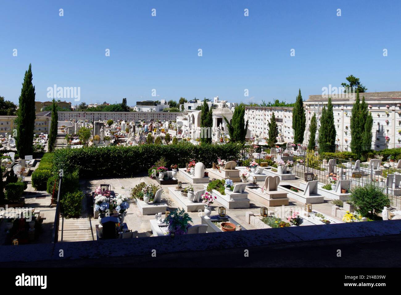 Cimitero tranquillo con pietre tombali ben disposte e fiori colorati sotto un cielo azzurro limpido con alberi che fiancheggiano i sentieri di Capri, Italia, Europa Foto Stock