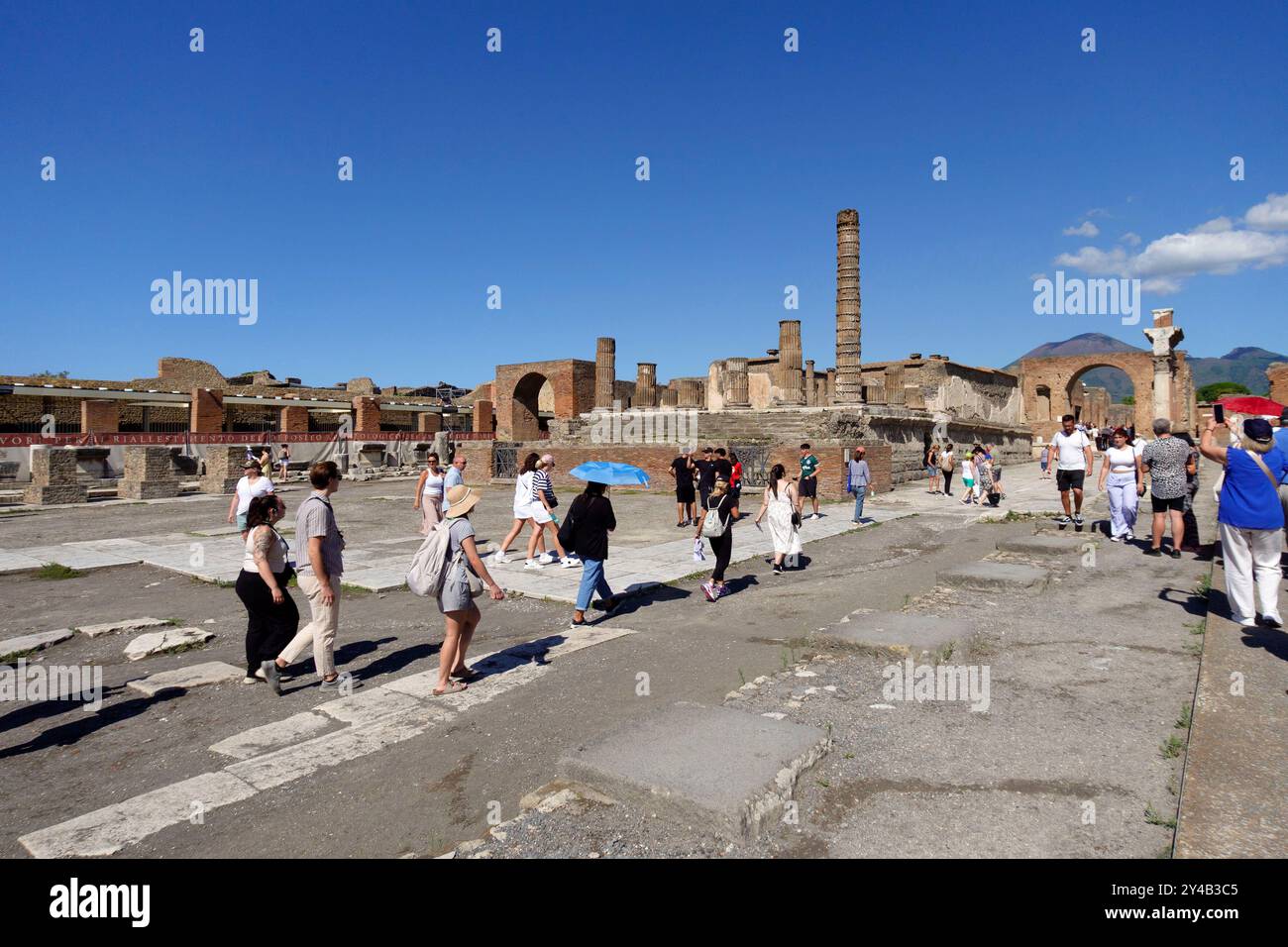 I turisti esplorano le antiche rovine di Pompei, in Italia, con cieli azzurri che evidenziano l'architettura storica e il Vesuvio in lontananza Foto Stock