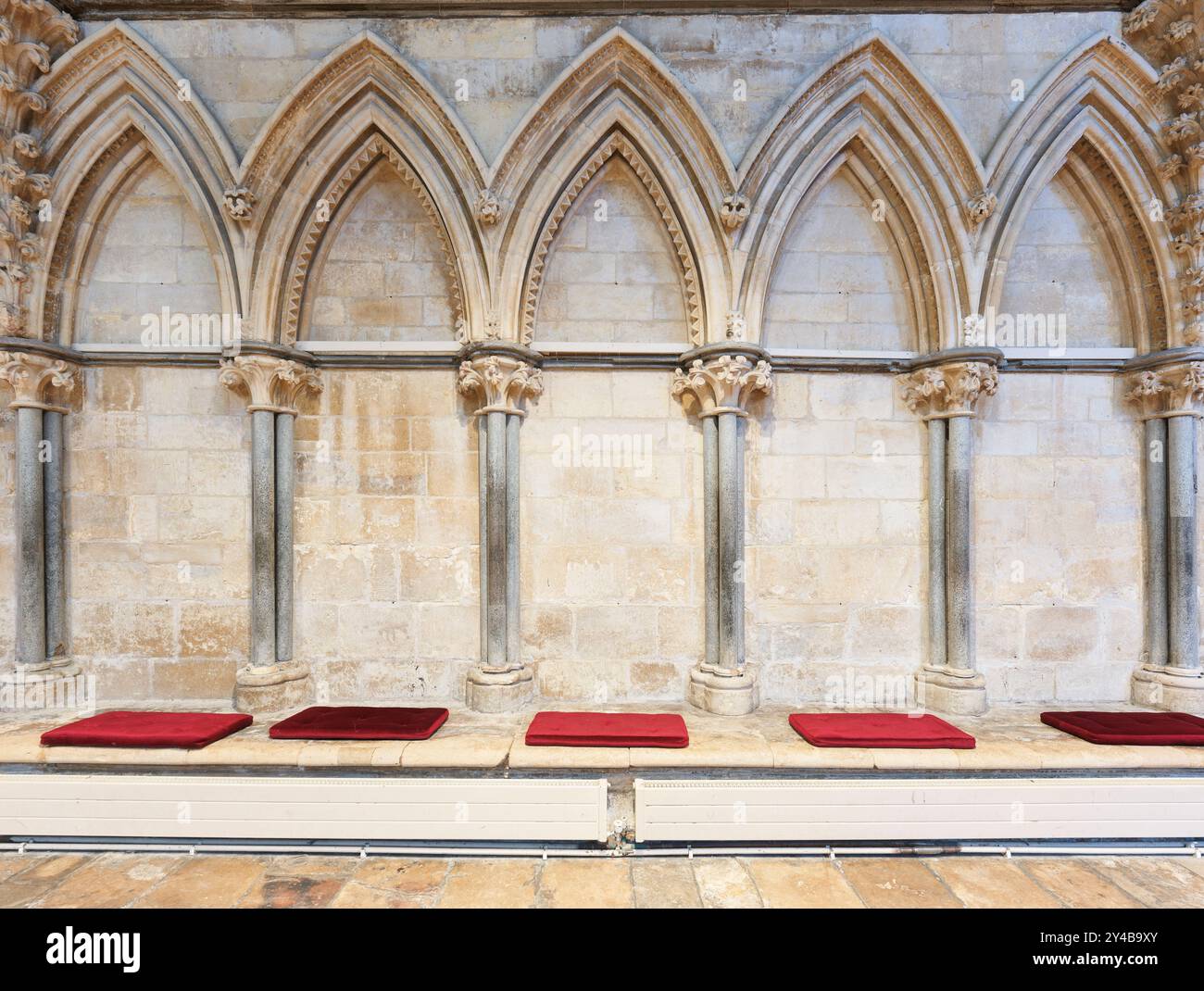 Cuscini rossi su sedili in pietra contro le pareti decorative della casa capitolare nella cattedrale di Lincoln, in Inghilterra. Foto Stock