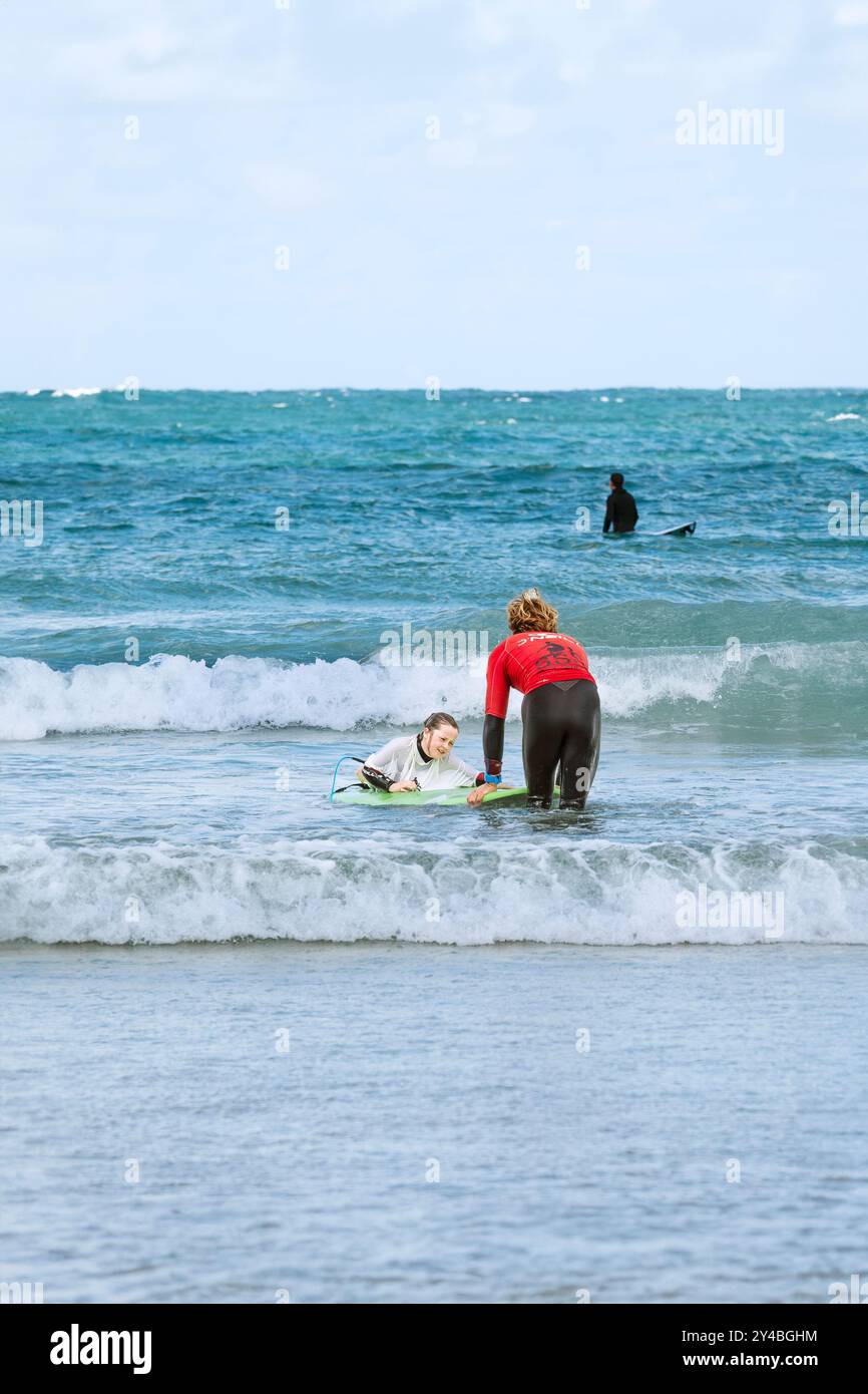Un giovane surfista principiante con un istruttore di surf che impara a fare surf a Towan Beach a Newquay in Cornovaglia nel Regno Unito. Foto Stock