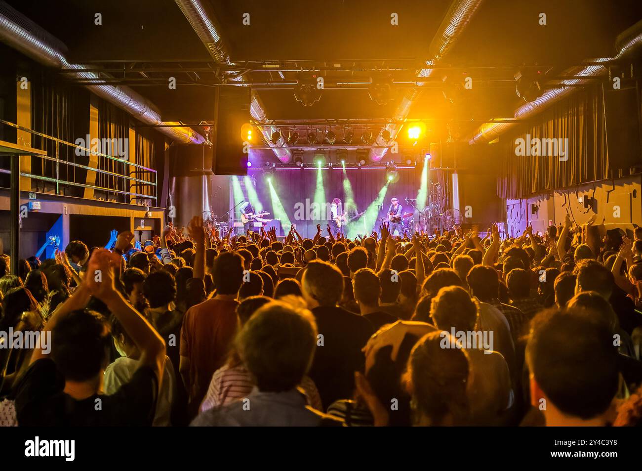 Dinamico concerto rock al coperto con un pubblico vivace e musicisti che si esibiscono su un palco ben illuminato, creando un'atmosfera energica piena di mu Foto Stock