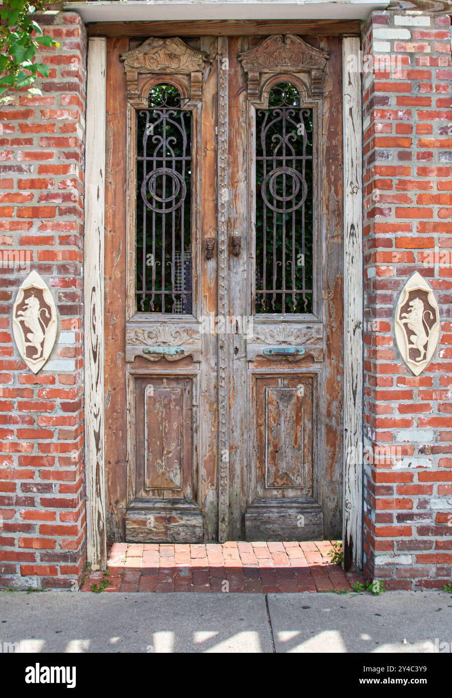 Antico ingresso doppio circondato da mattoni con inserti decorativi. La porta è intemprata e ha finestre sbarrate Foto Stock