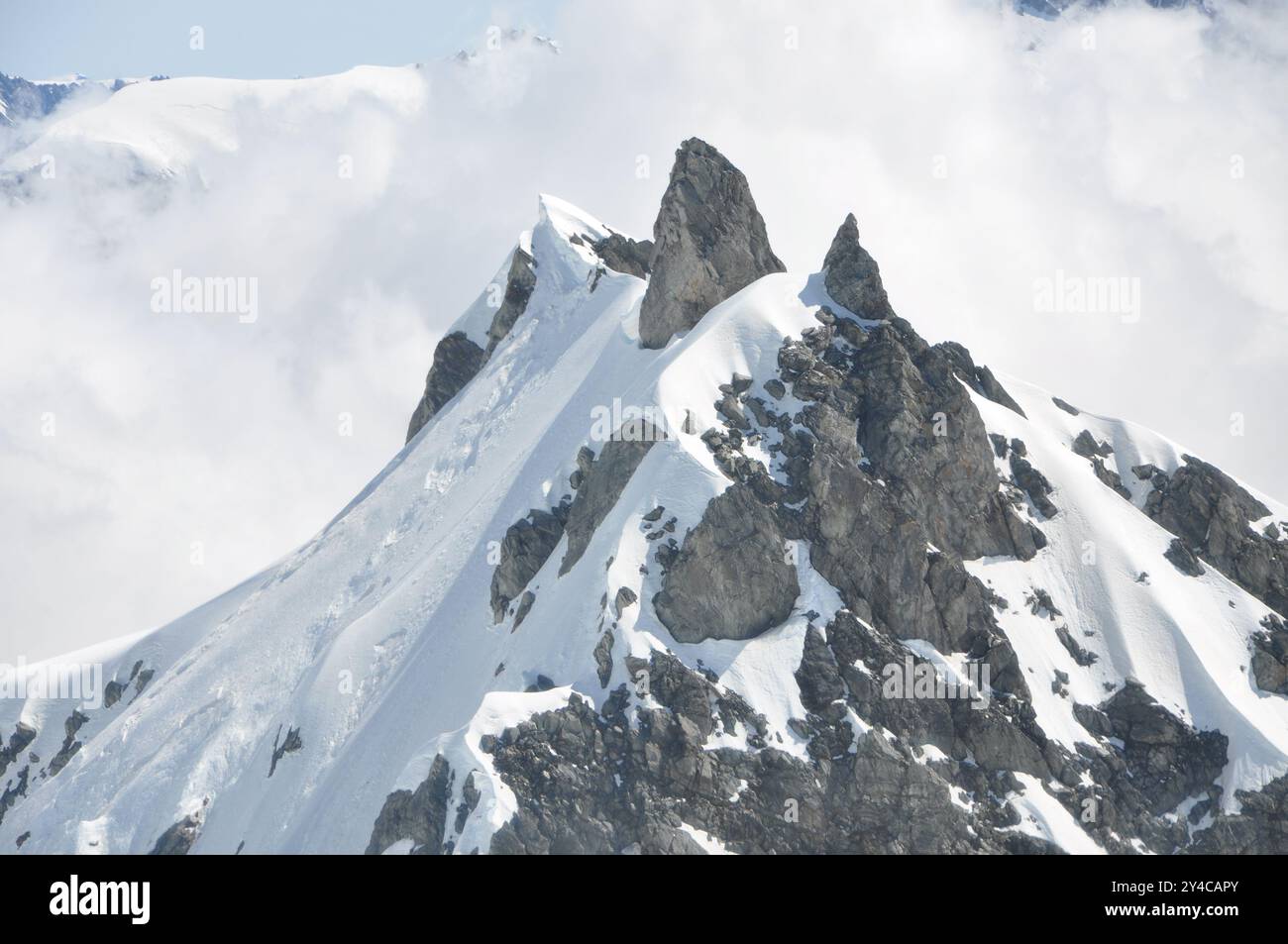 Cima rocciosa ricoperta di neve in un mare di nuvole Foto Stock