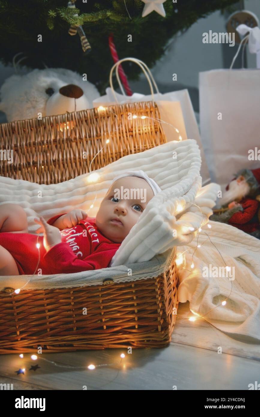 Un bambino appena nato con abiti natalizi che dorme in un cestino sul pavimento con decorazioni natalizie. Capodanno Foto Stock