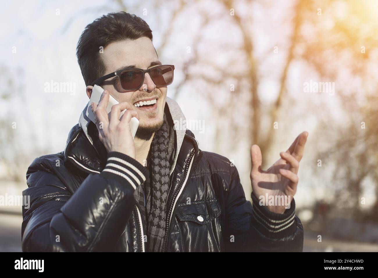 Un ragazzo in una giacca calda con uno smartphone in mano, una giornata di sole Foto Stock