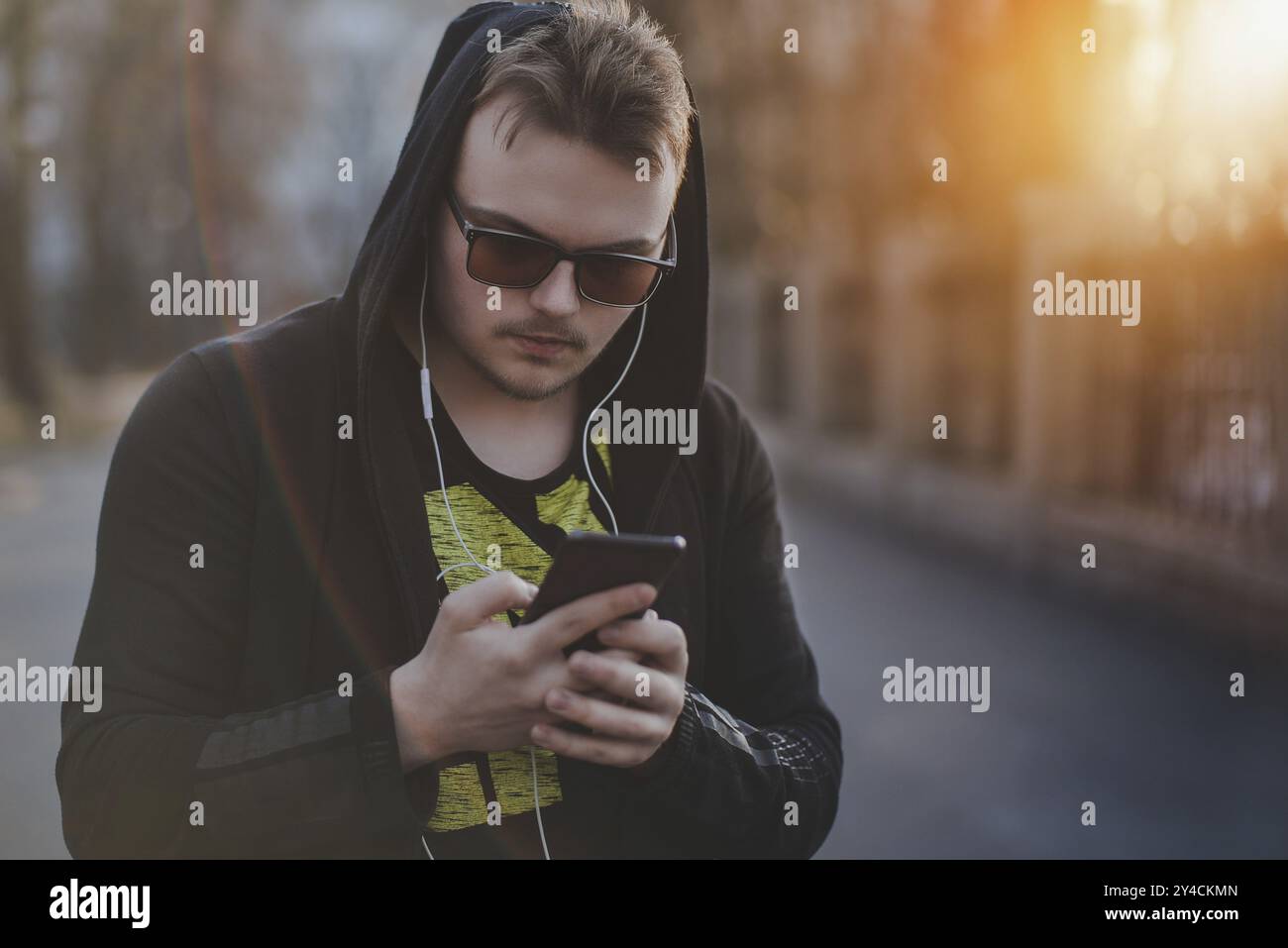 Uomo in Hood con le cuffie che guarda lo smartphone Foto Stock