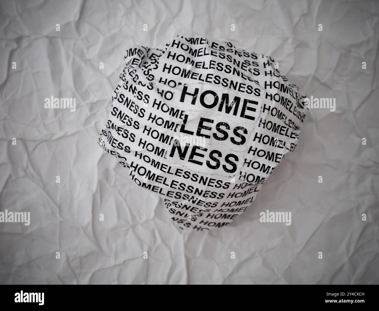 Palla di carta sgualcita con parole Homelessness su uno sfondo strappato di pezzi di carta bianca. Foto Stock