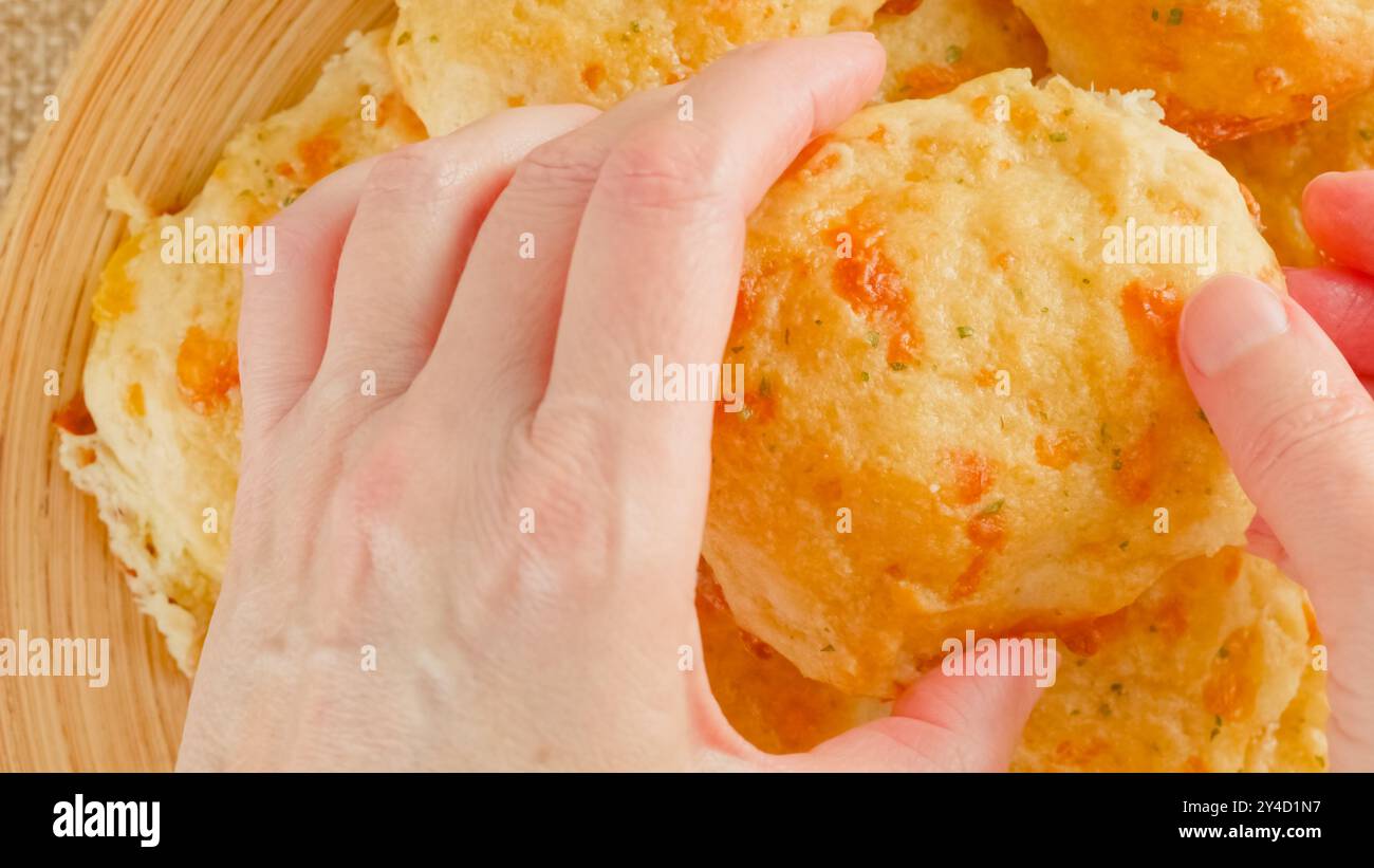 Biscotti al formaggio con burro e aglio condimento primo piano su un piatto di legno, vista dall'alto, mani di donna Foto Stock