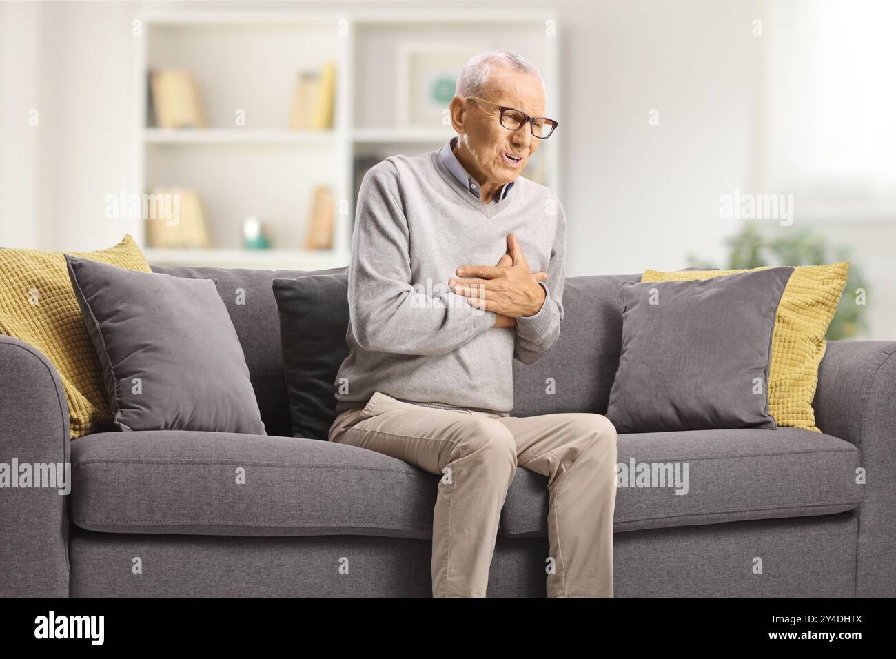 Uomo anziano che soffre di infarto su un divano in soggiorno Foto Stock