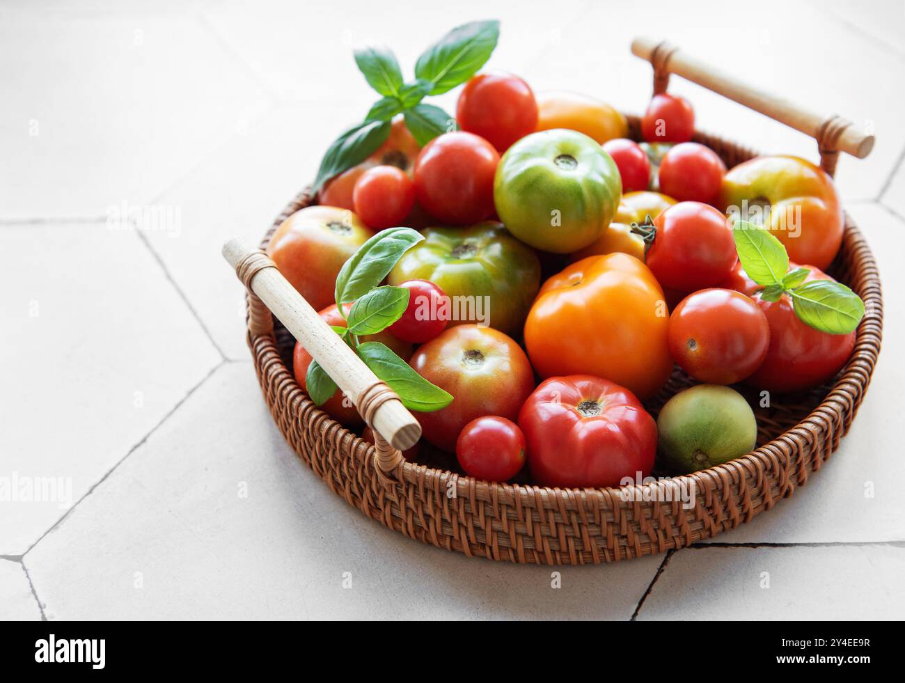 Un'abbondante collezione di pomodori colorati riempie un cesto intrecciato, caratterizzato da varie dimensioni e sfumature che si appoggiano su un ripiano della cucina a fine estate Foto Stock