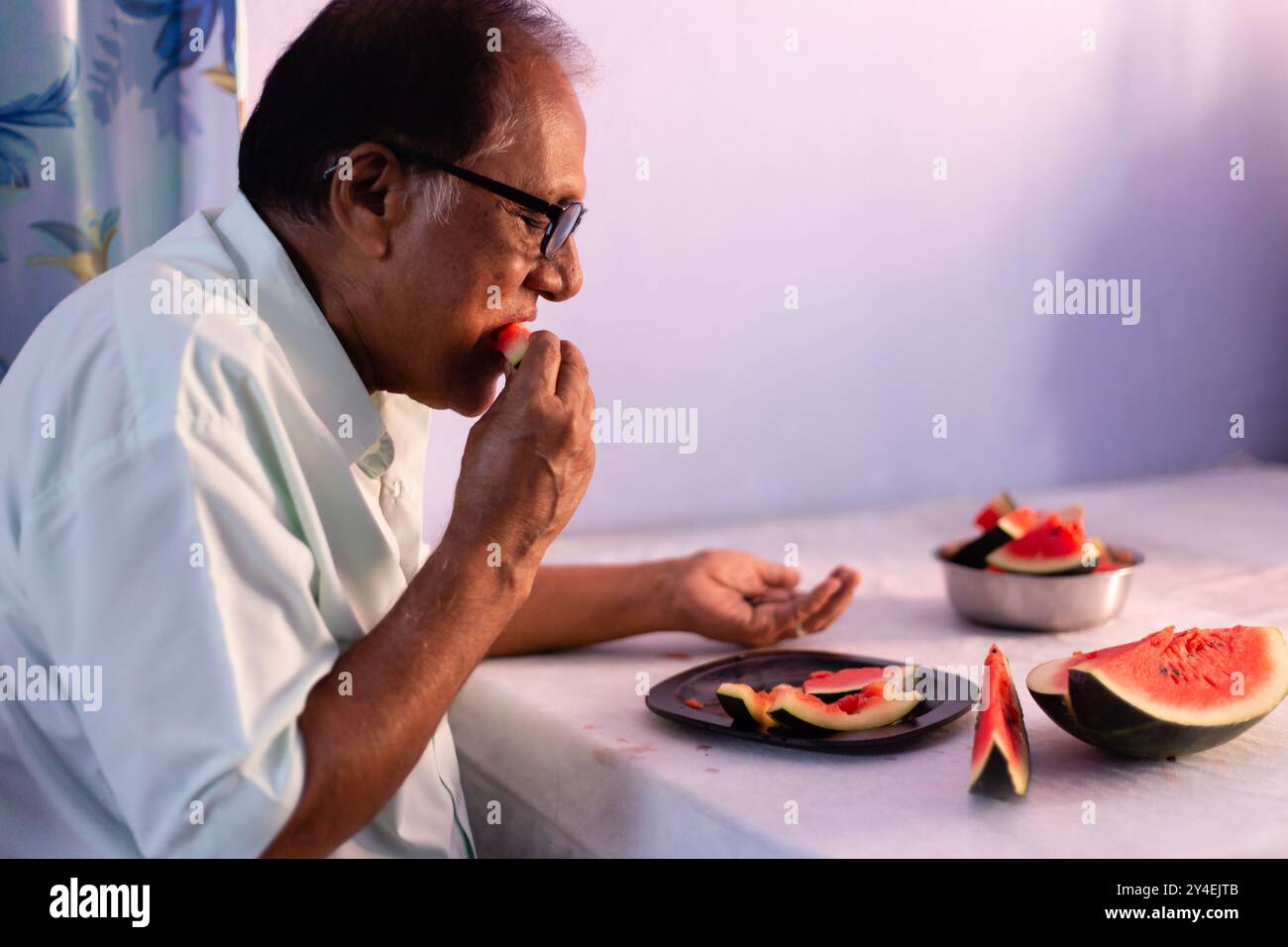 Un uomo indiano anziano che mangia melone rosso succoso a casa in casa Foto Stock