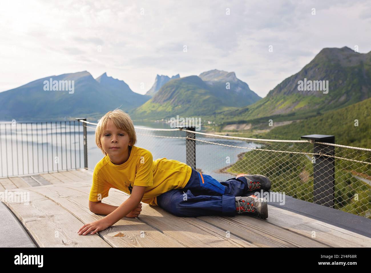 I bambini, in piedi sul bordo di una piattaforma panoramica lunga 44 metri, si affacciano sull'acqua del Bergsfjord, godendosi la vista sull'isola di Senja, nord nord nord Foto Stock