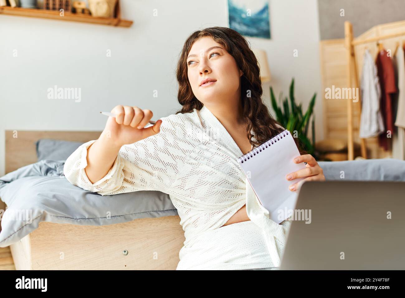 Una giovane donna di grandi dimensioni si rilassa a casa, sfoggiando idee nel suo notebook con un look pensivo. Foto Stock