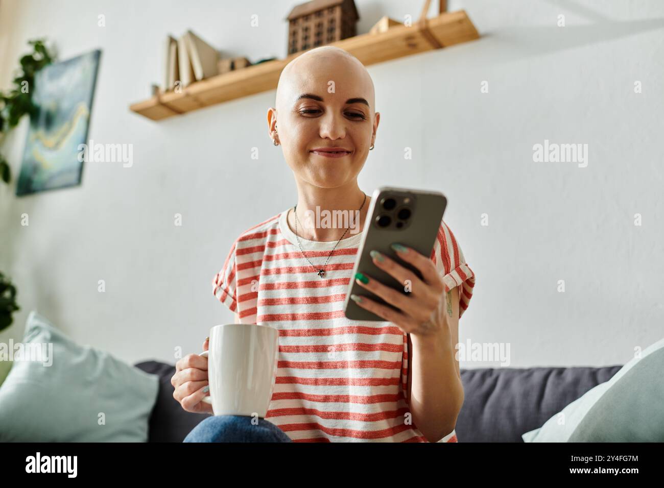Una donna allegra e calva gusta il caffè mentre è impegnata con il suo smartphone, trasudando calore. Foto Stock