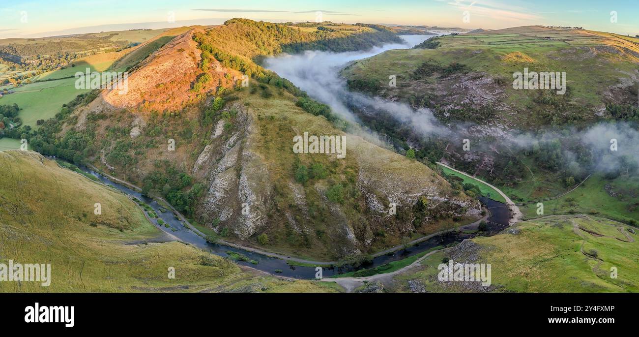 Un sottile strato di nebbia scorre attraverso la valle mentre il sole mattutino illumina la collina. Dovedale Peak District Derbyshire Regno Unito Foto Stock