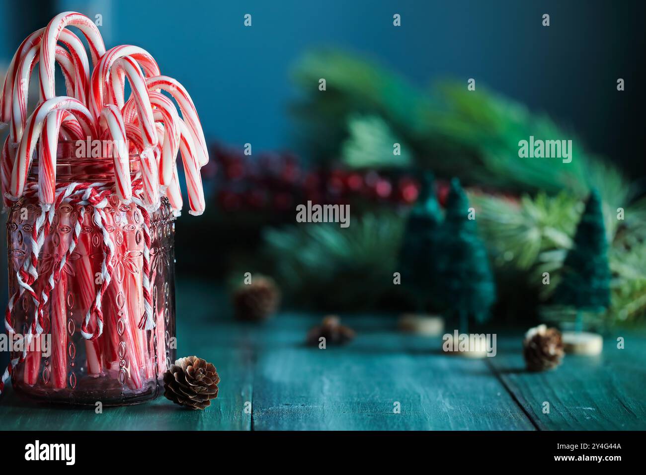 barattolo mason rosso legato con spago e riempito con bastoncini di caramelle alla menta piperita. Decorazioni natalizie e rami sul retro. Messa a fuoco selettiva con sfondo sfocato. Foto Stock