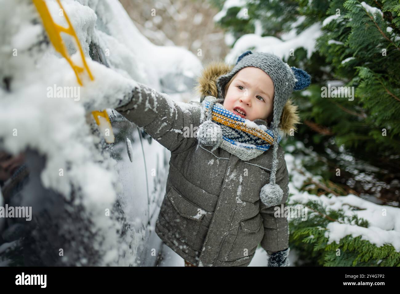 Adorabile bambino che aiuta a spazzolare la neve da un'auto. Il piccolo aiutante della mamma. Attività invernali per bambini piccoli. Foto Stock