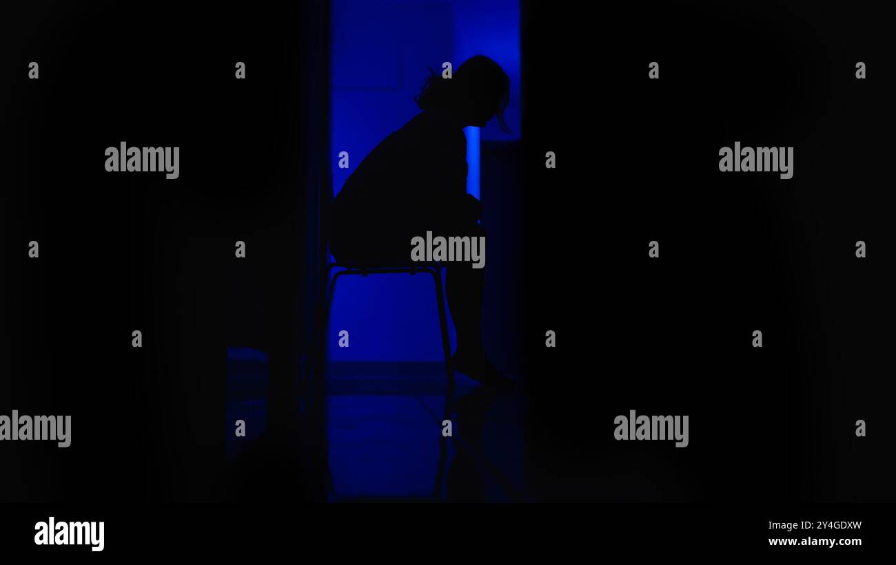 Immagine minimalista in tonalità blu che ritrae una persona di profilo, seduta su una sedia, immersa in pensieri profondi. Cattura un momento di solitudine e rif Foto Stock