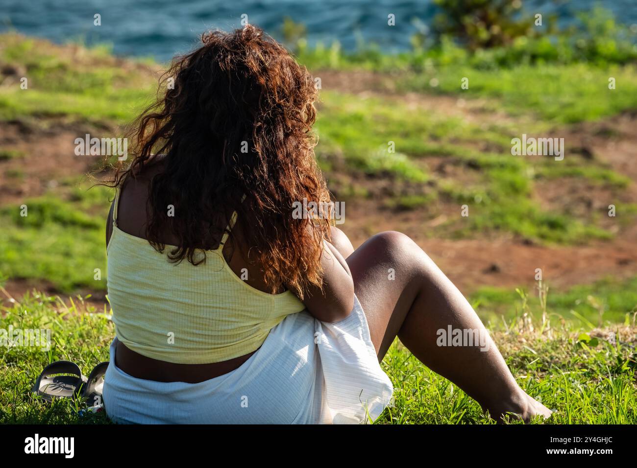 La donna si rilassa nell'erba durante il tramonto. Una giovane donna, più grande afroamericana che si rilassa all'aperto nel parco estivo, abbracciando la positività del corpo. H Foto Stock
