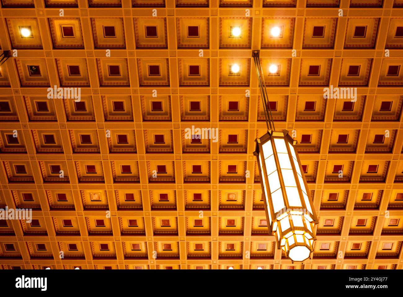 30th Street Station soffitto a cassettoni Philadelphia Pennsylvania // PHILADELPHIA, Pennsylvania — il motivo geometrico del soffitto a cassettoni della 30th Street Station di Philadelphia presenta apparecchi di illuminazione sospesi appesi a pannelli incassati. Il soffitto in stile neoclassico e art déco fa parte dell'atrio principale di questa storica stazione ferroviaria, che funge da importante nodo di trasporto per i servizi ferroviari Amtrak e SEPTA. Progettata dallo studio di architettura Graham Anderson Probst & White, la stazione è stata completata nel 1933 durante la grande depressione ed è elencata nella National Reg Foto Stock