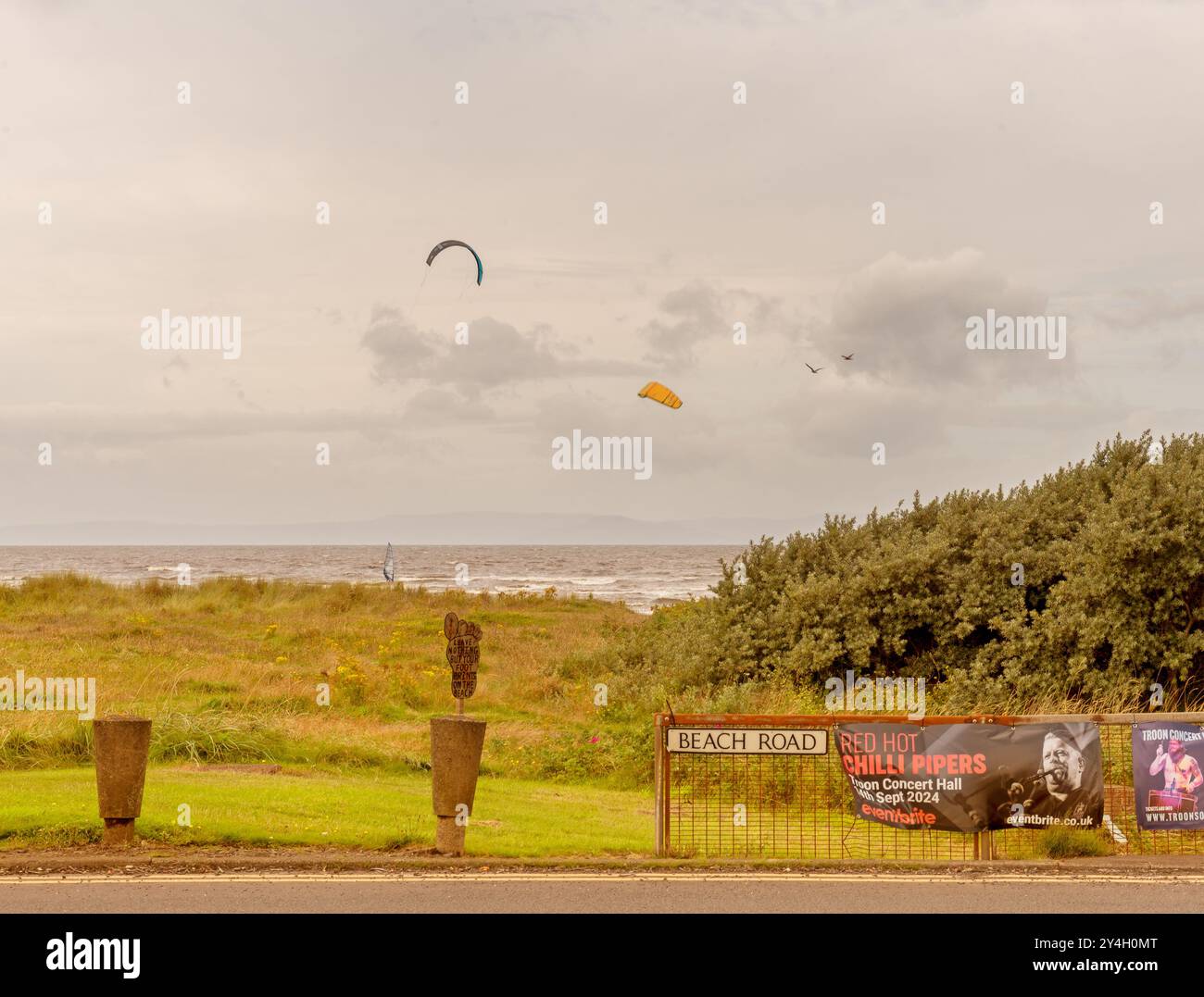 Un cartello per Beach Road con kitesurf in lontananza a Barassie Beach, vicino a Troon in Scozia durante un'estate ventosa nel 2024 Foto Stock