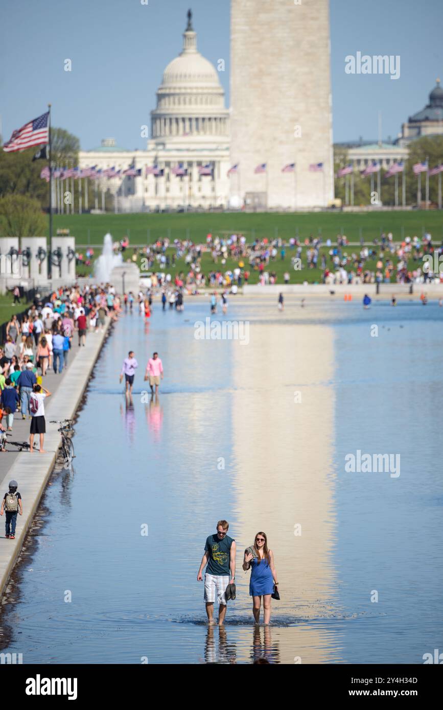 Lincoln Memorial Reflecting Pool Washington Monument Washington D.C. // WASHINGTON, D.C. - i visitatori si riuniscono lungo il Lincoln Memorial Reflecting Pool sul National Mall, approfittando del tempo caldo per godersi il sito iconico. La piscina lunga 2.029 metri, che ha subito un importante restauro completato nel 2012, crea un'immagine speculare del Monumento a Washington visibile sullo sfondo. La cupola del Campidoglio degli Stati Uniti può essere vista in lontananza, completando la vista storica che forma il nucleo cerimoniale della capitale della nazione. Foto Stock