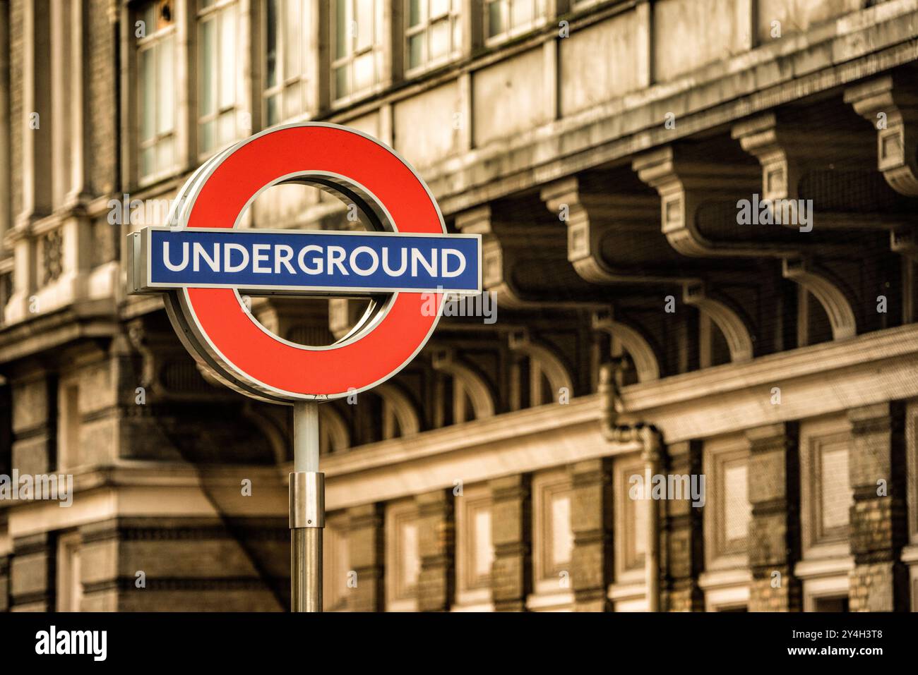 London Underground Roundel Sign London England // LONDON, United Kingdom - l'iconico cartello rotondo della metropolitana di Londra, caratterizzato da un cerchio rosso con una barra orizzontale blu, segna l'ingresso di una stazione della metropolitana. Il simbolo distintivo è servito come logo principale per il sistema di trasporto pubblico di Londra sin dalla sua introduzione nel 1908, evolvendosi dai disegni precedenti fino a diventare uno degli emblemi di transito più riconosciuti al mondo. La metropolitana di Londra, comunemente chiamata metropolitana, opera come il più antico sistema metropolitano del mondo, avendo aperto la sua prima linea nel 1863. I trasporti per Londra mantengono questa e Foto Stock