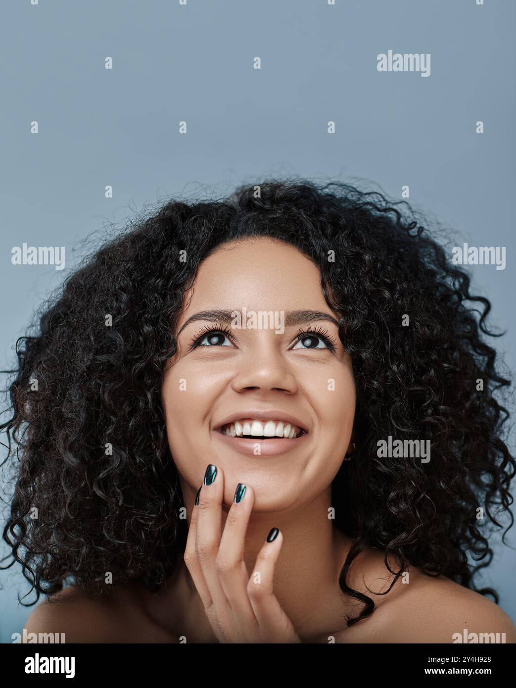 Primo piano di una giovane donna felice che guarda in alto. Ritratto di donna con capelli ricci sorridenti e rivolti verso l'alto. Foto Stock
