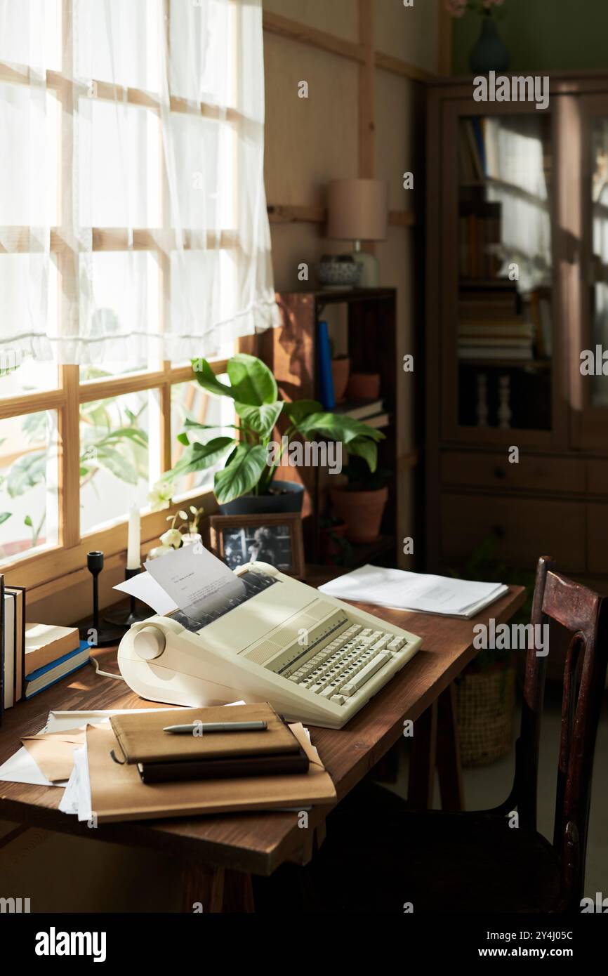 La luce del sole scorre attraverso la finestra illuminando il computer retrò con documenti e libri su una scrivania in legno, creando un'atmosfera nostalgica e produttiva Foto Stock