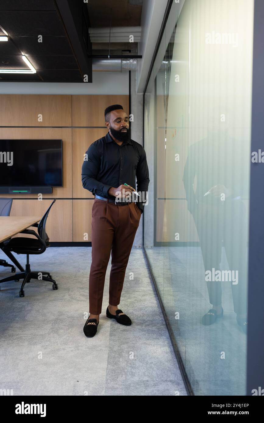 Uomo d'affari afroamericano in ufficio che scrive su una parete di vetro durante la riunione, tenendo un cartello Foto Stock