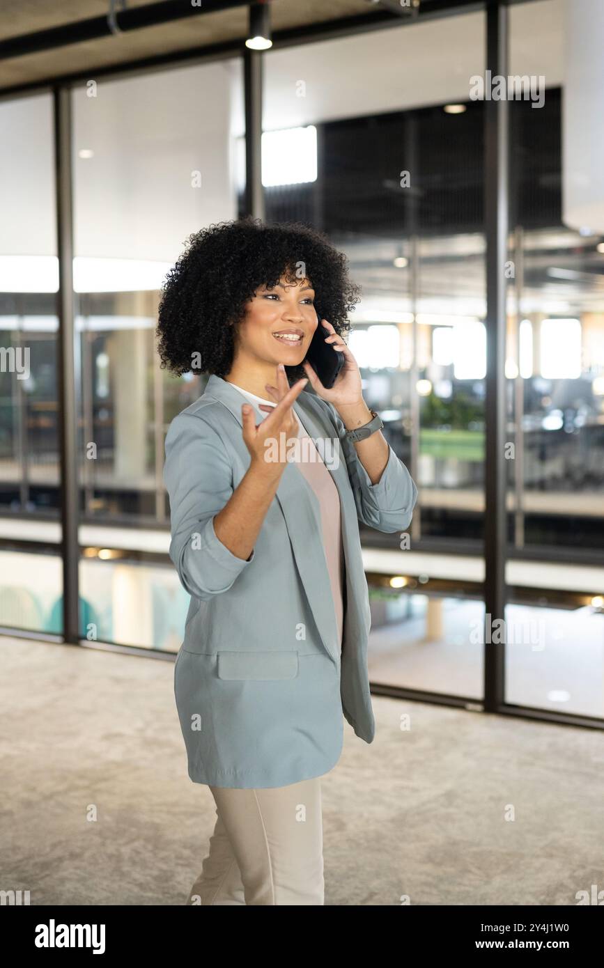 Parla con smartphone, una donna d'affari che cammina in un ufficio moderno, gesti con sicurezza Foto Stock