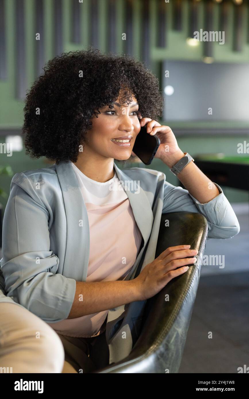 Parla con smartphone, donna in abito da lavoro seduta in un ufficio moderno Foto Stock