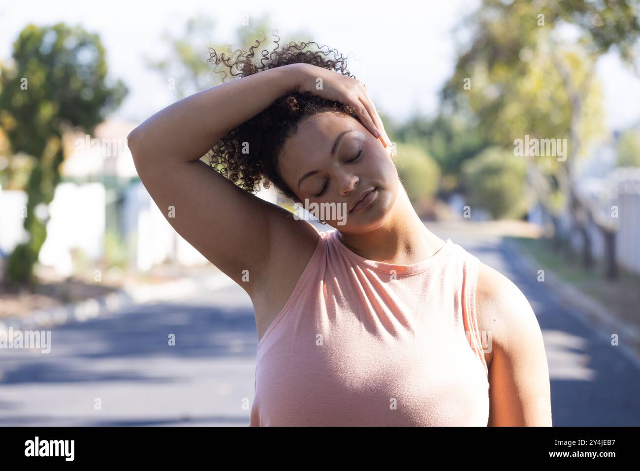 Allungamento dei muscoli del collo, donna con capelli ricci che si rilassa all'aperto nella giornata di sole nel parco Foto Stock