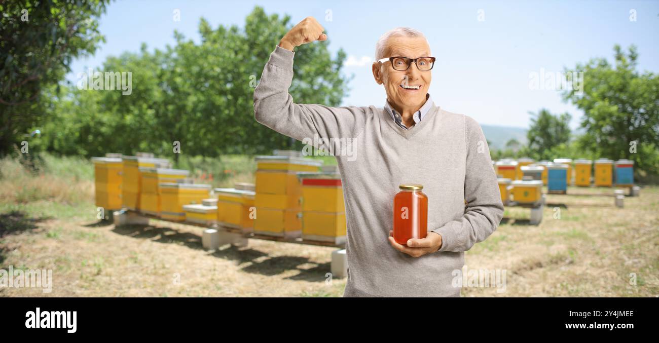 Un uomo anziano forte che tiene in mano un vaso di miele in un allevamento di api Foto Stock