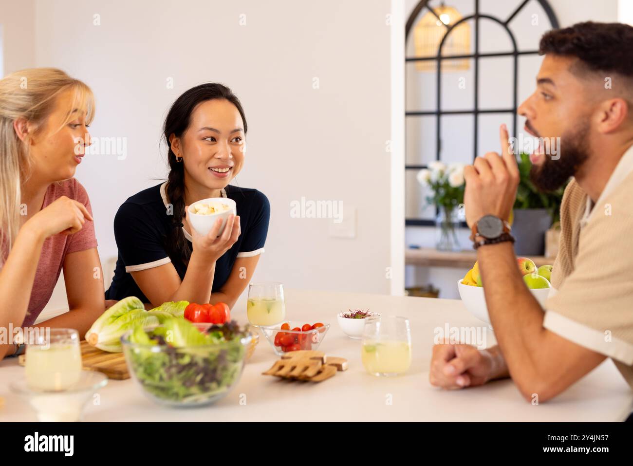 Amici che si godono un pasto sano e chiacchierano intorno al tavolo della cucina con insalata Foto Stock