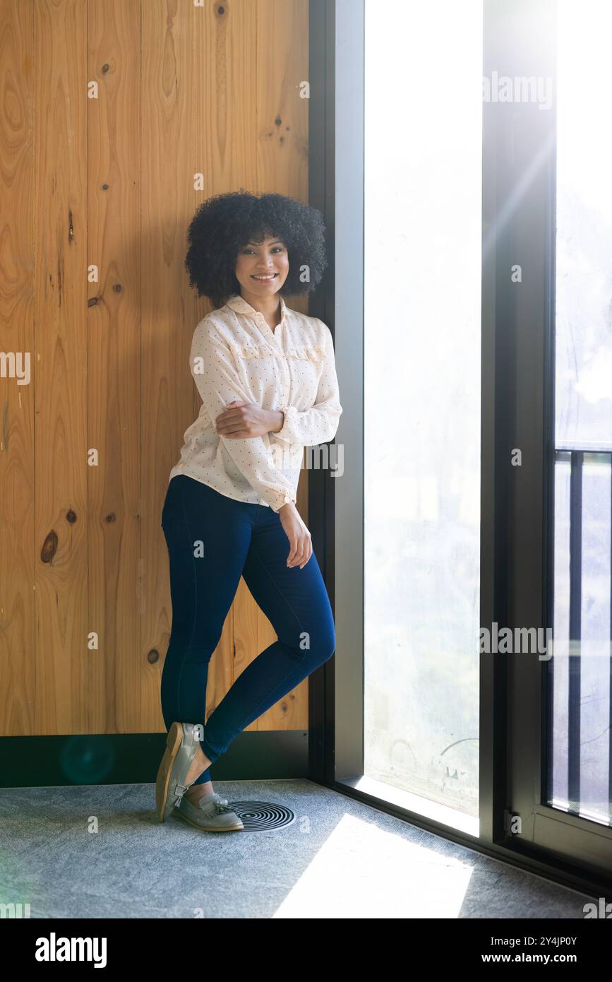 Donna sorridente in piedi accanto alla finestra, indossa un abbigliamento casual in ufficio Foto Stock