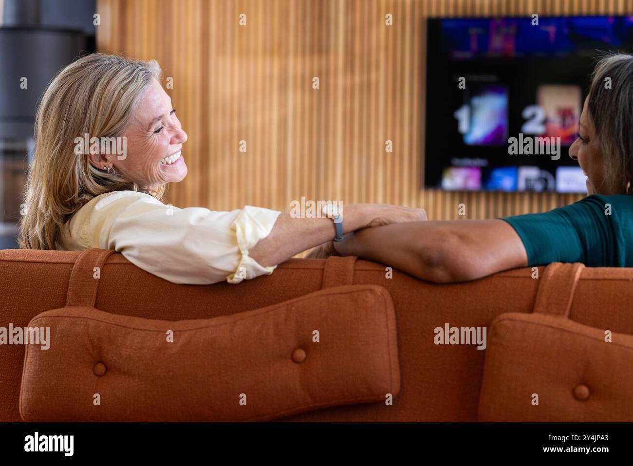 A casa, sorridenti amiche di sesso femminile multirazziale sedute sul divano, a guardare la tv e a conversare Foto Stock