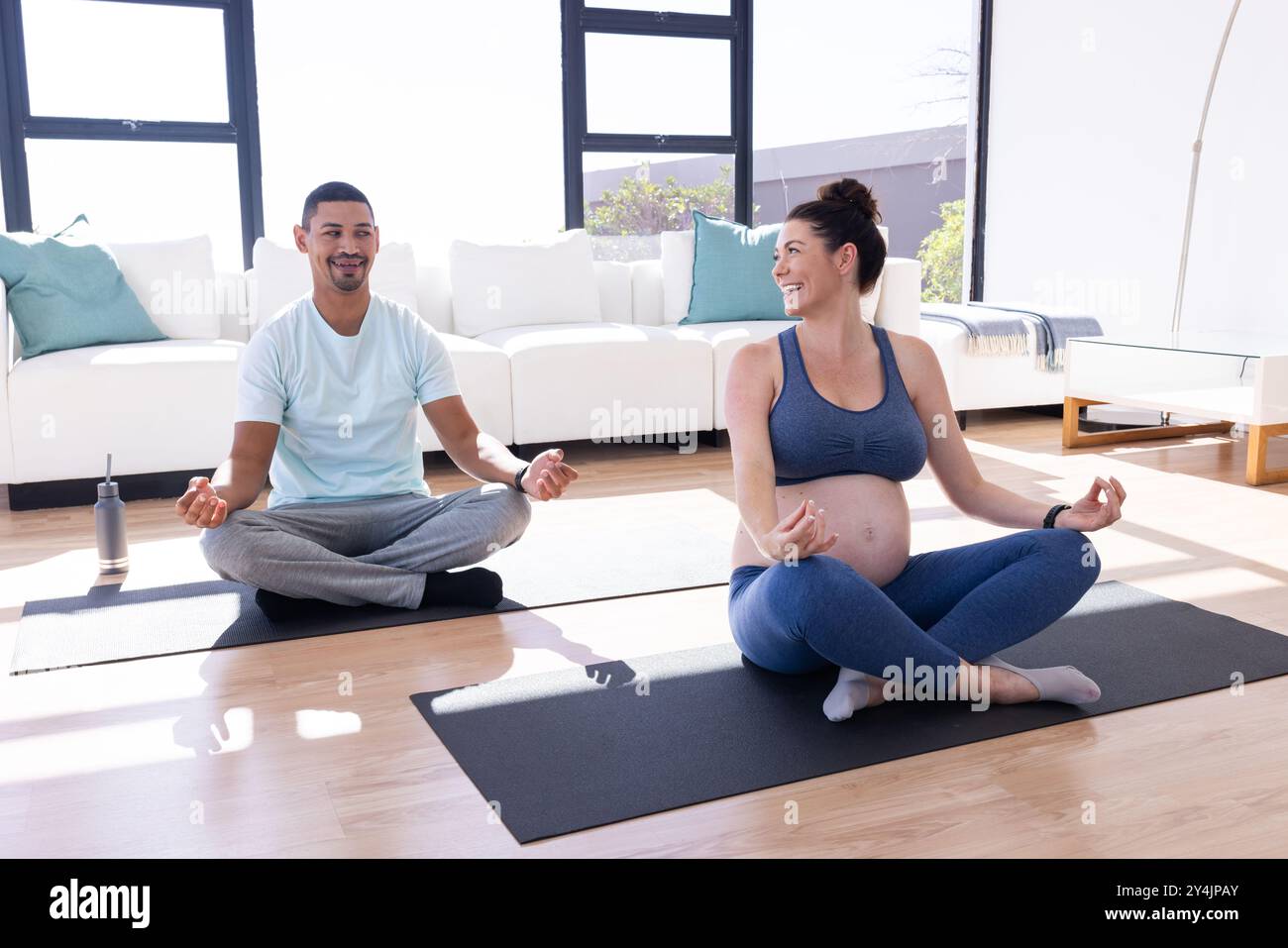 A casa, coppia multirazziale, pratica yoga prenatale, donna incinta e partner su tappetini da yoga Foto Stock