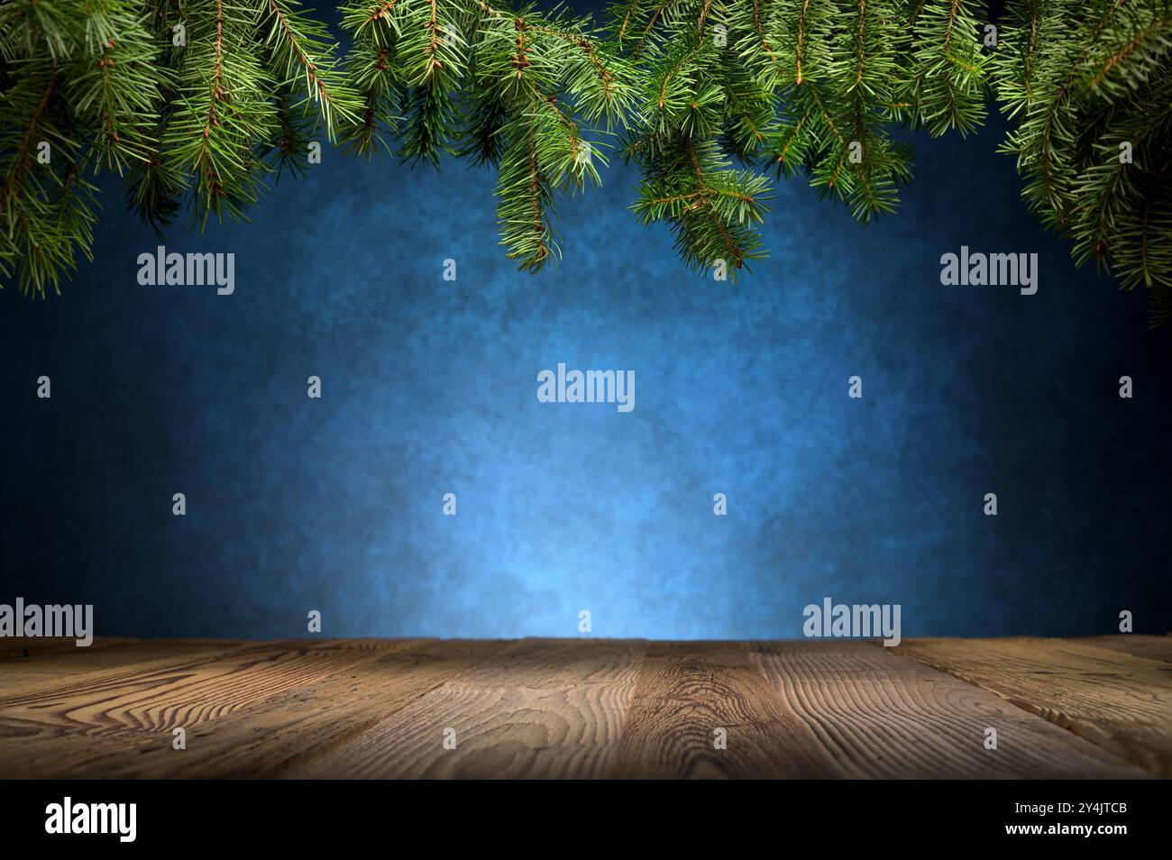 Design dello sfondo del piano portapaziente per Natale o altro. Un'elegante scena da studio con rami di abete e tavole di legno che incorniciano uno sfondo con vignettature blu Foto Stock