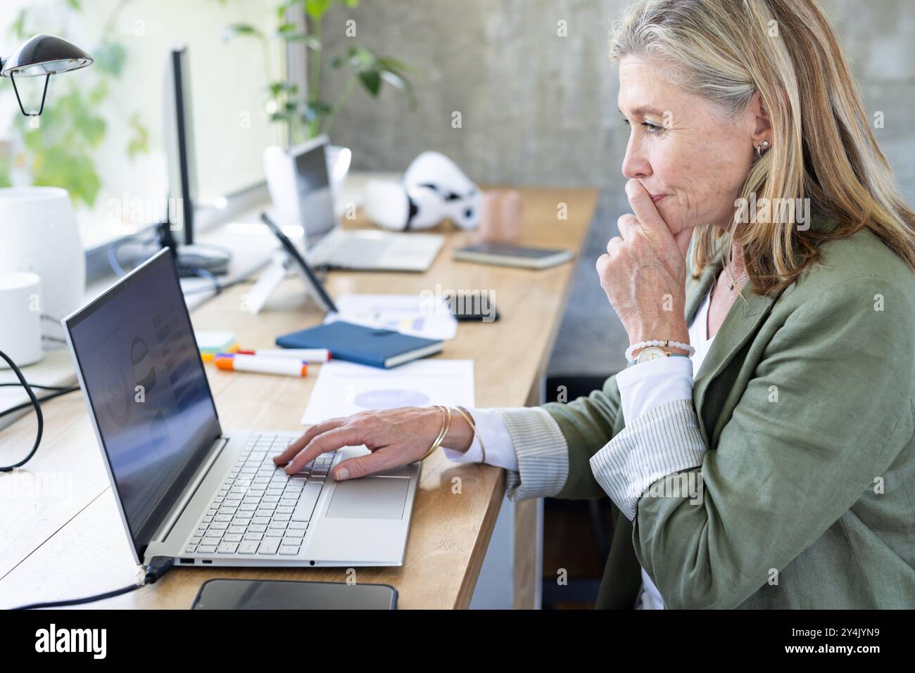 Lavora su un notebook, donna anziana che si concentra alla scrivania con forniture per ufficio Foto Stock