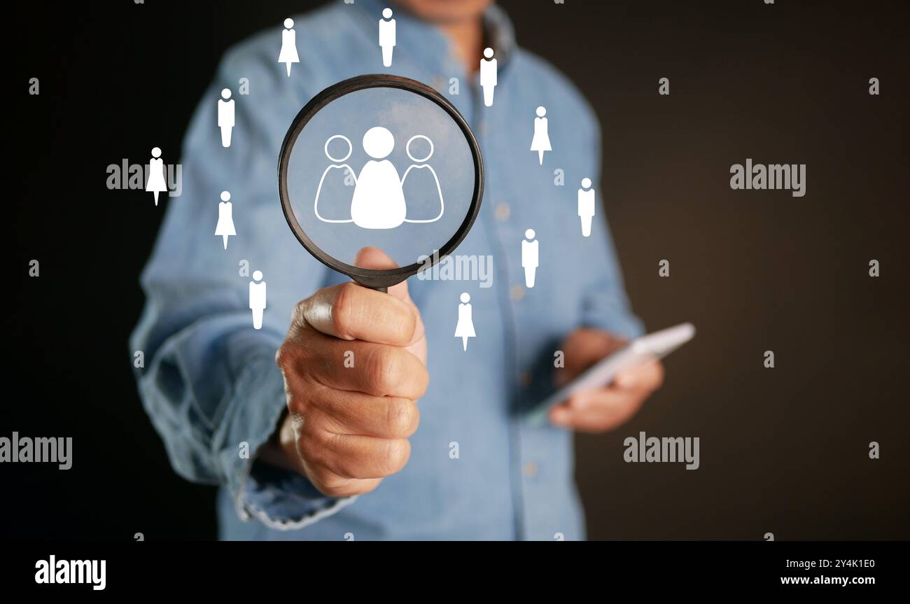 CRM o Customer Relationship Management e HRM. Un uomo utilizza una lente di ingrandimento per trovare l'icona delle persone per il gruppo di destinazione focalizzato sul cliente, i social media e Foto Stock