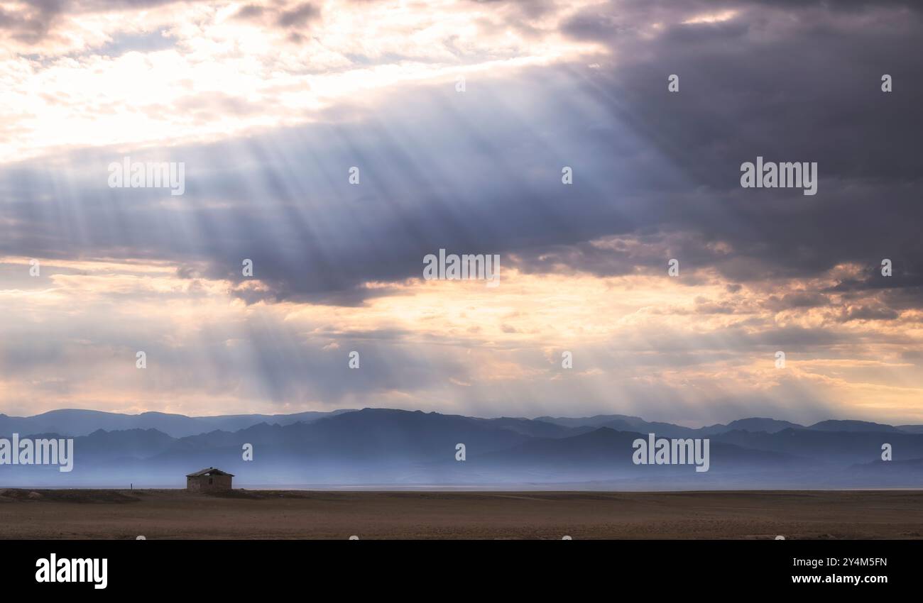 piccola casa di argilla solitaria nel deserto, nelle steppe o nelle praterie sotto un cielo nuvoloso con raggi di sole Foto Stock