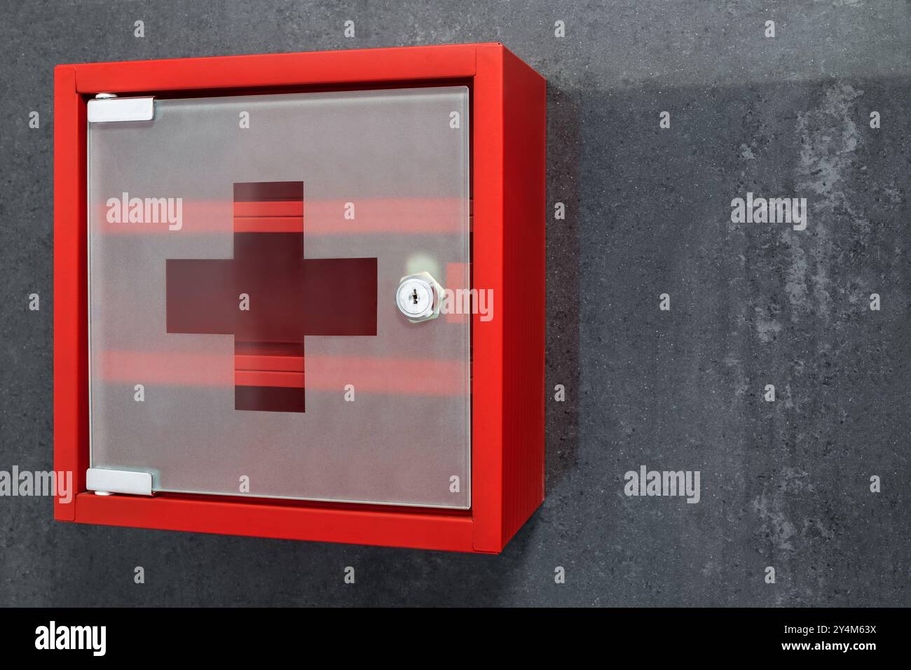 Armadio medico vuoto in metallo rosso chiuso appeso su sfondo grigio scuro della parete. Vista in prospettiva Foto Stock