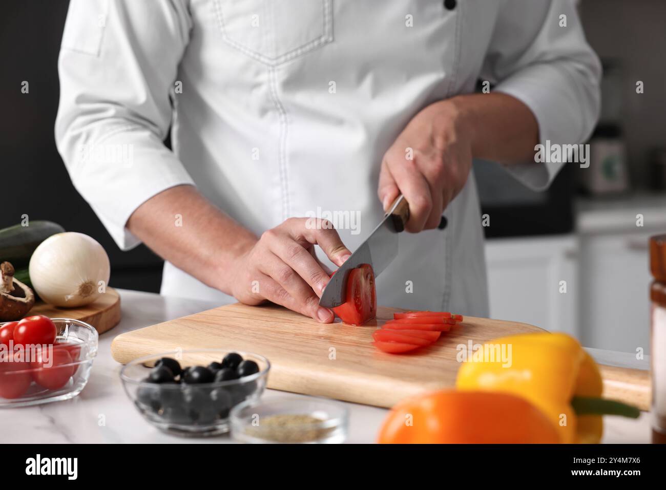 Chef professionista che taglia il pomodoro a tavola in cucina, primo piano Foto Stock