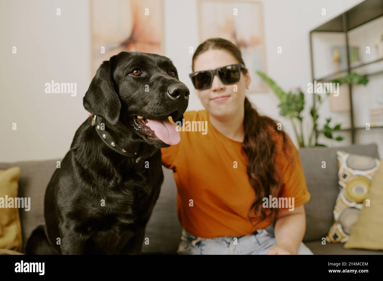 Primo piano medio del Labrador nero e del suo proprietario che riposano sul divano mentre posano per un ritratto insieme Foto Stock