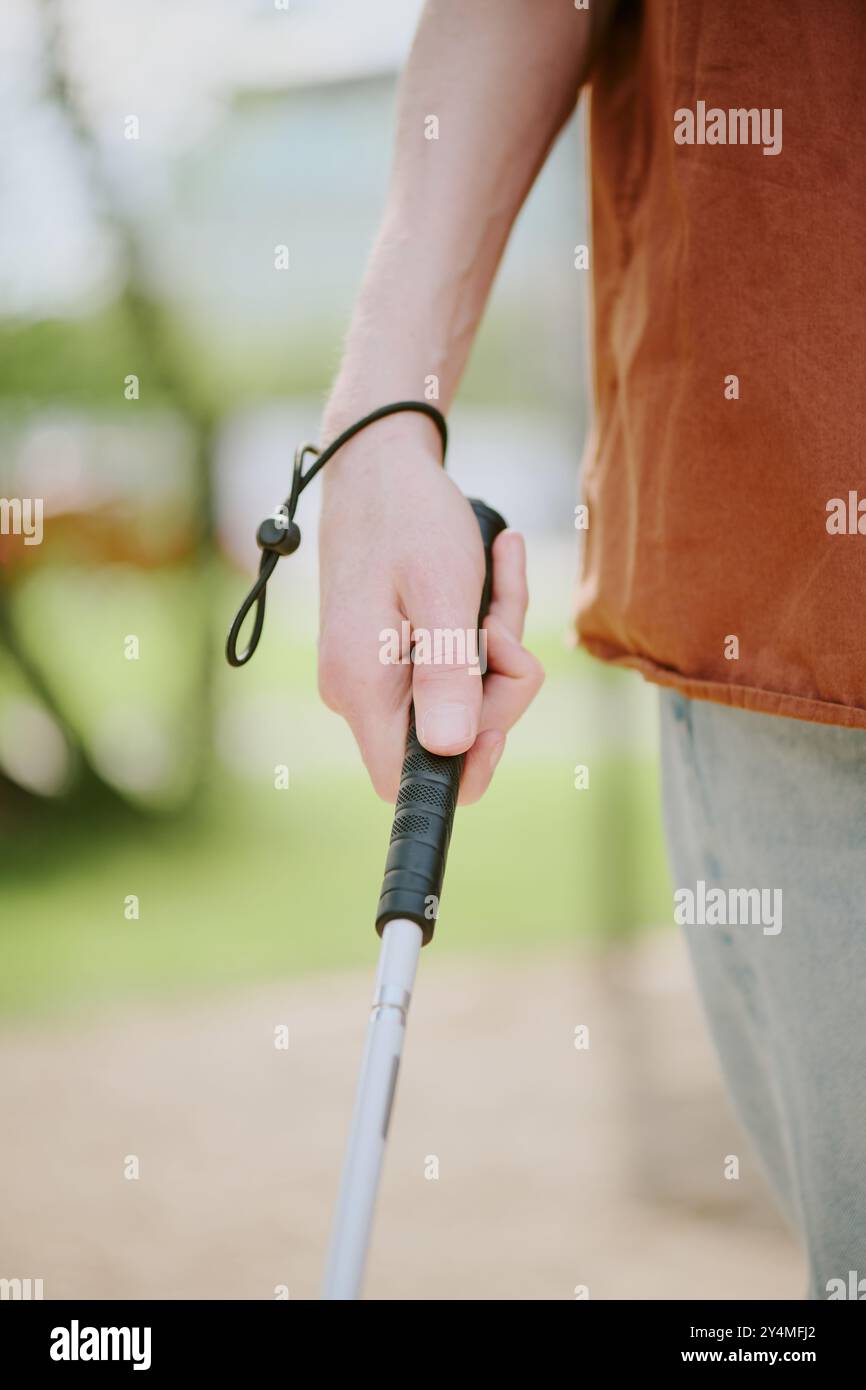 Immagine da vicino verticale di una mano maschile irriconoscibile che tiene in mano un bastone metallico per camminare nel parco Foto Stock