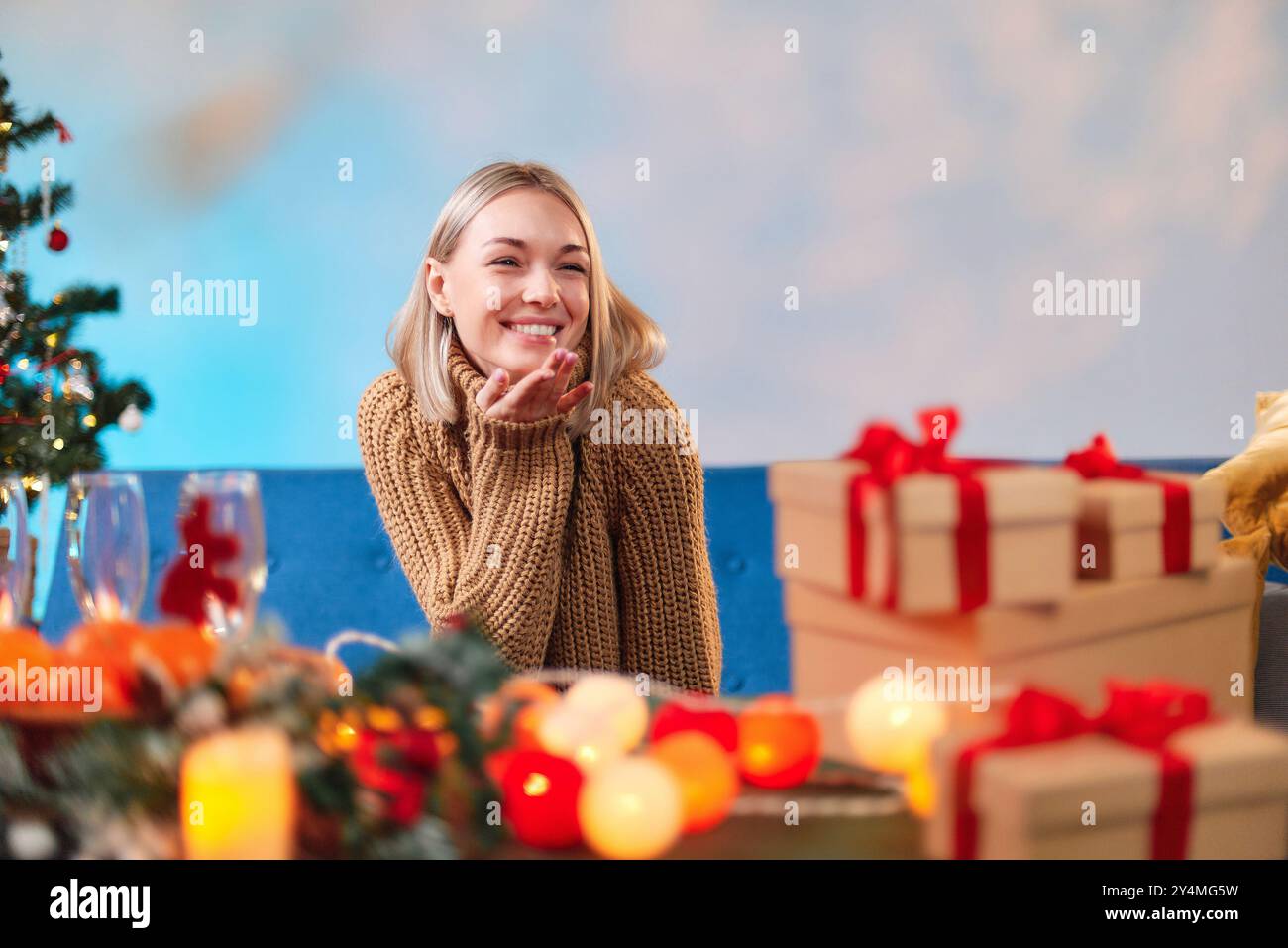Donna che manda un bacio d'aria mentre prepara il suo tavolo per la cena di Natale con regali e decorazioni natalizie. Foto Stock