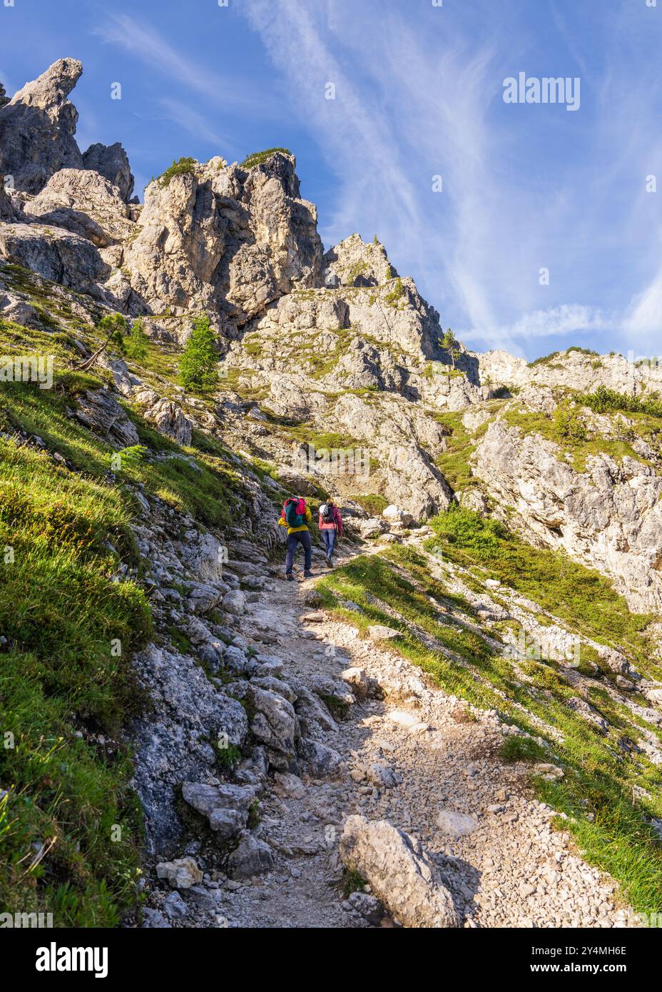 Uomo che cammina, donna con zaini. Arrampicatori su sentieri in montagna che vanno a scalare. Bellissimo paesaggio con gente, alte rocce, sentieri, gras verdi Foto Stock